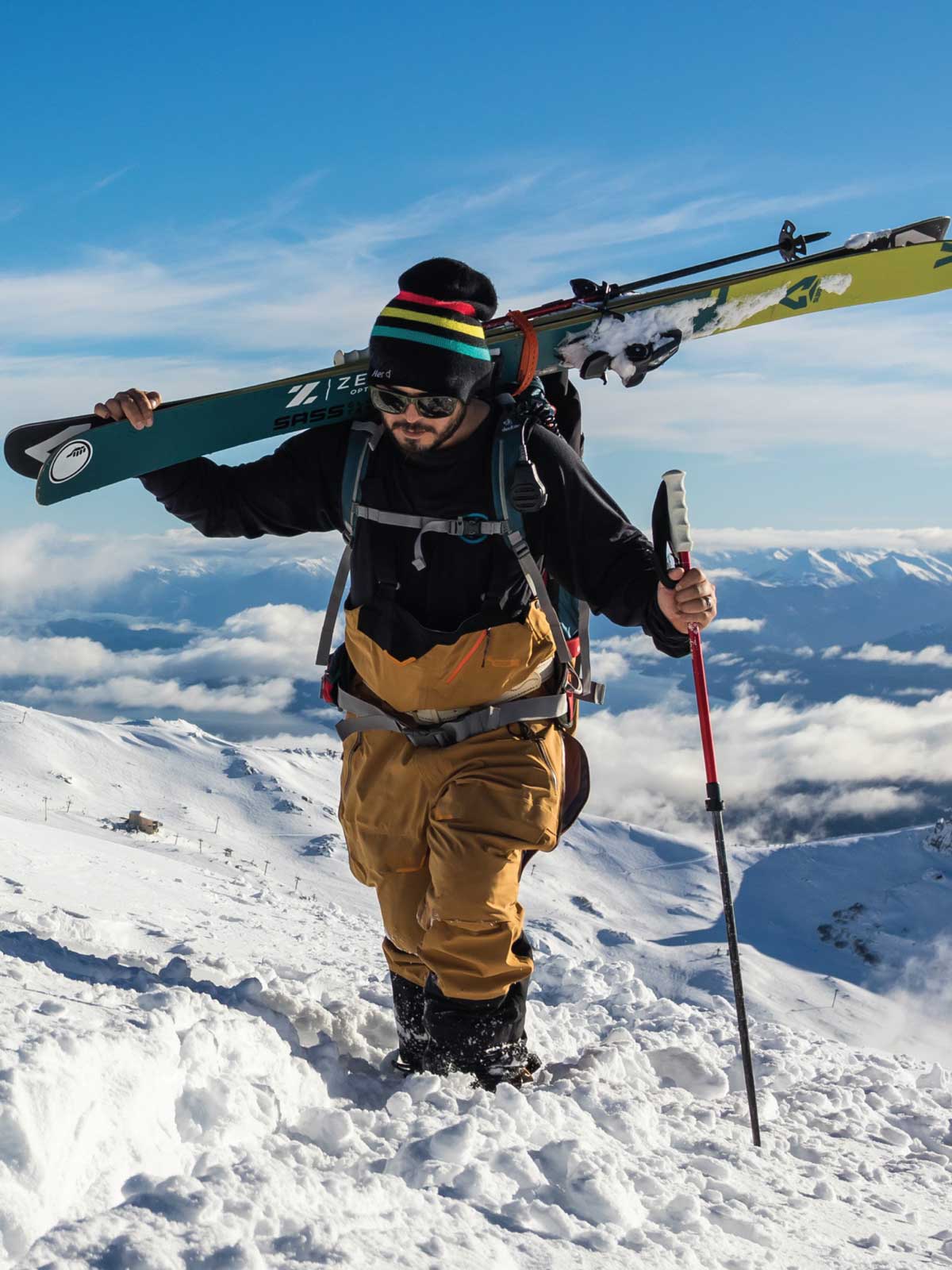 Man hiking up mountain with skis on his shoulder